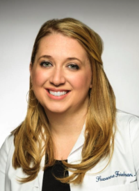 Woman with long blonde hair smiling in black top and white coat